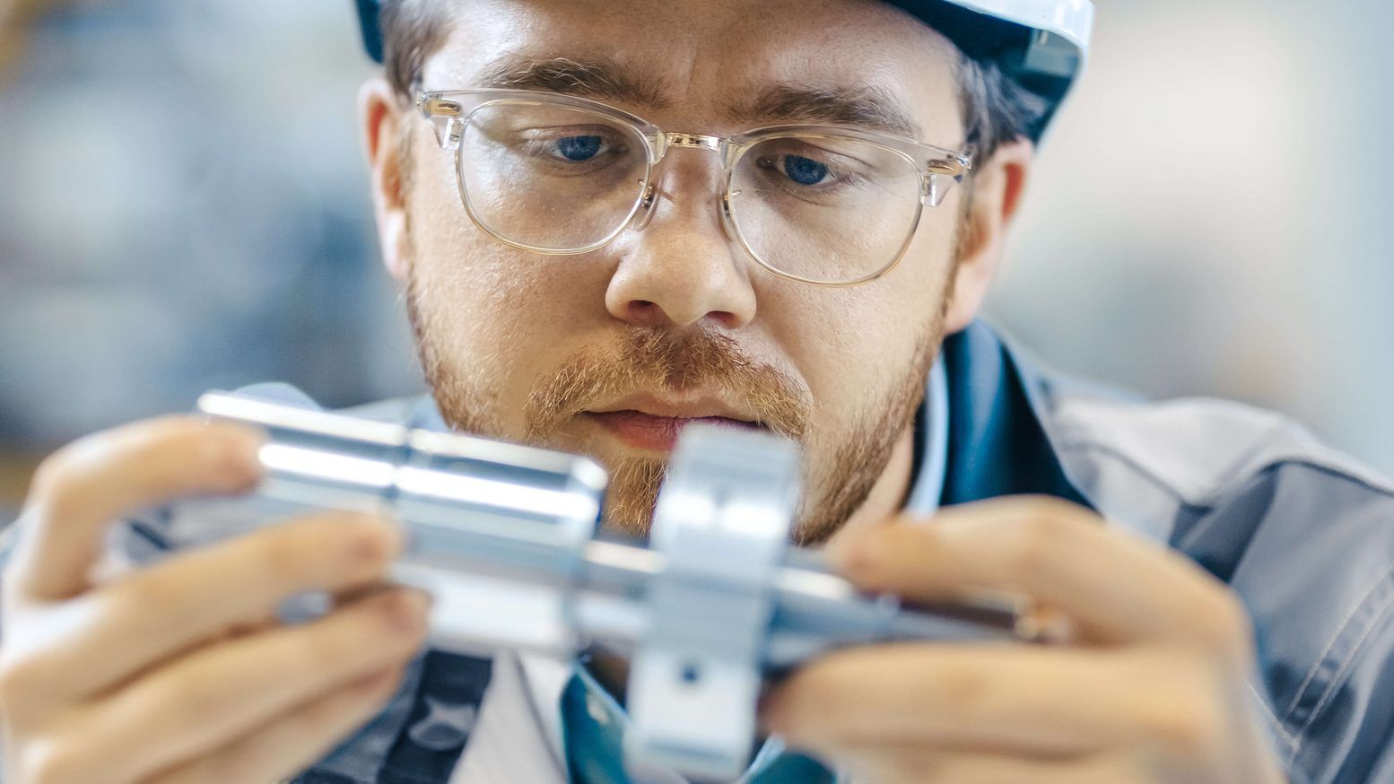 Mitarbeiter mit Schutzbrille prüft ein Bauteil