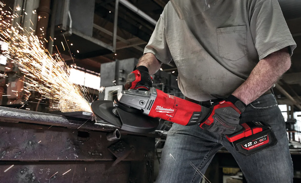 Handwerker trennt Metall mit einem Akku-Winkelschleifer, Funkenflug in einer Werkhalle