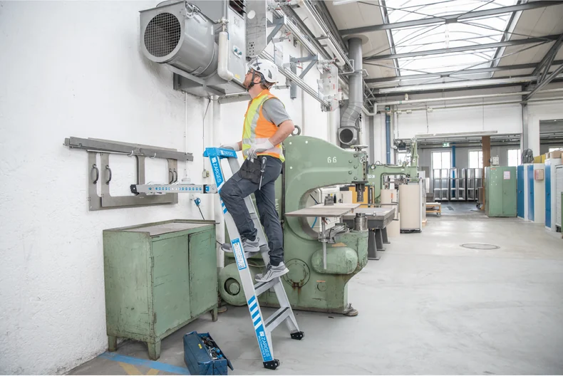 Beschäftigte auf einer Stufenleiter an einer Maschine in einer Produktionshalle, Katalog-Anwendungsbild